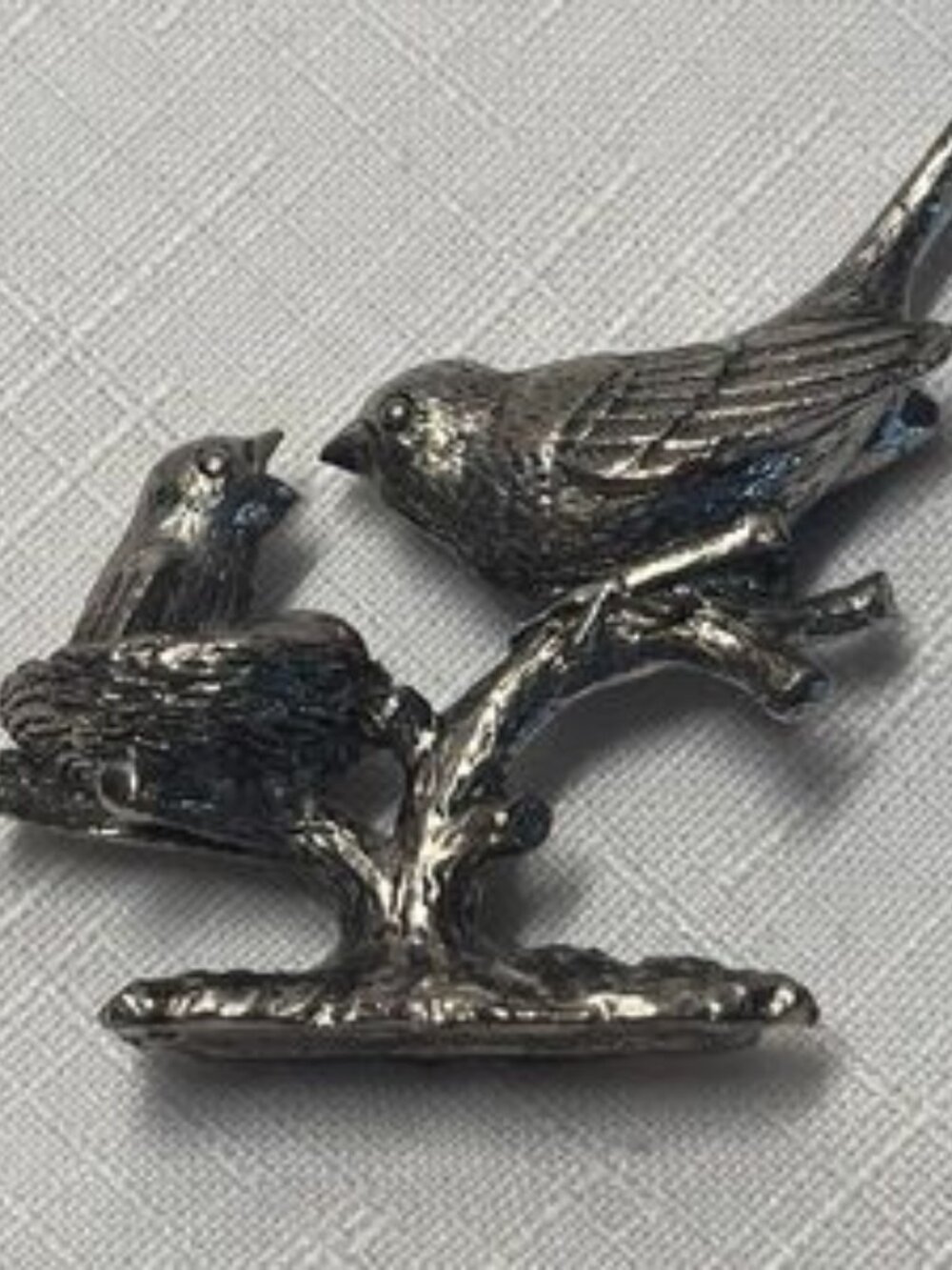 pewter figurine features a parent bird feeding a chick in a nest. high detail